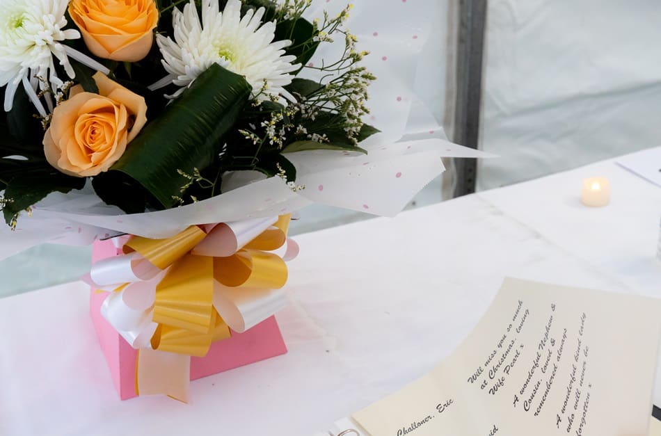 A book of remembrance on a table covered with a white table cloth and a bouquet of white and yellow flowers in the background