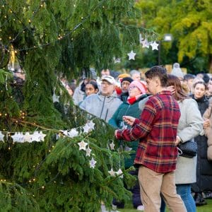 A man placing a dedication on a Christmas tree decorated in memory of loved ones, surrounded by a crowd