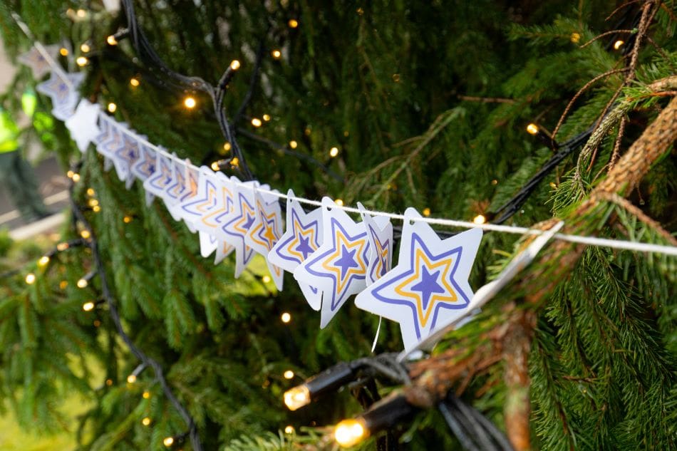 Paper star decorations hanging on a Christmas tree with twinkling lights in the background