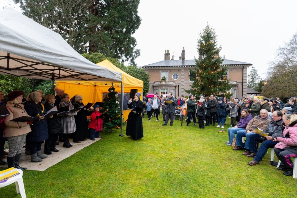 A crowd gathered in front of a Christmas tree listening to a choir singing