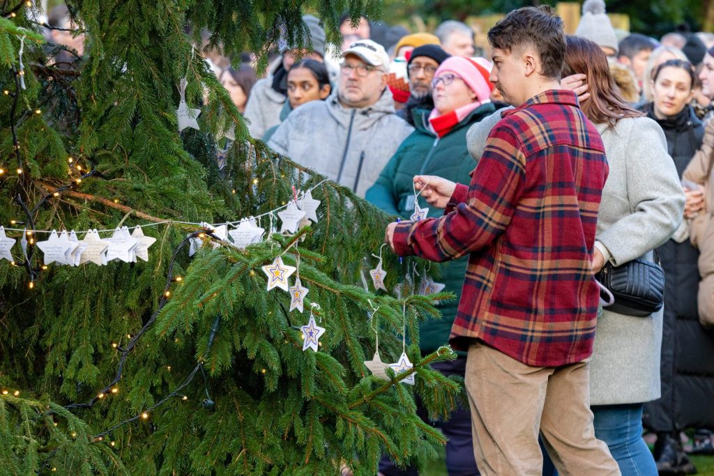 A man hanging a decoration on the Tree of Life with a group of people behind him