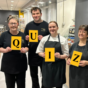 A group of Compton's Cafe colleagues hold a sign saying "quiz"